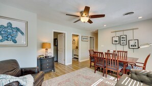 A living room with a brown leather couch, a patterned rug, a wooden dining table with chairs, a ceiling fan, and framed pictures on the wall. - Beachy Wilmington Home: 6 Mi to Riverwalk + Dtwn! (Wilmington)