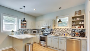 A modern kitchen with white cabinets, a central island, stainless steel appliances, and a tiled backsplash. - Beachy Wilmington Home: 6 Mi to Riverwalk + Dtwn! (Wilmington)
