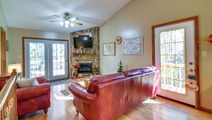 A spacious living room with a stone fireplace, a leather sofa, and a television. - Burnside Resort Cabin w/ Hot Tub & Outdoor Spots! (Burnside)