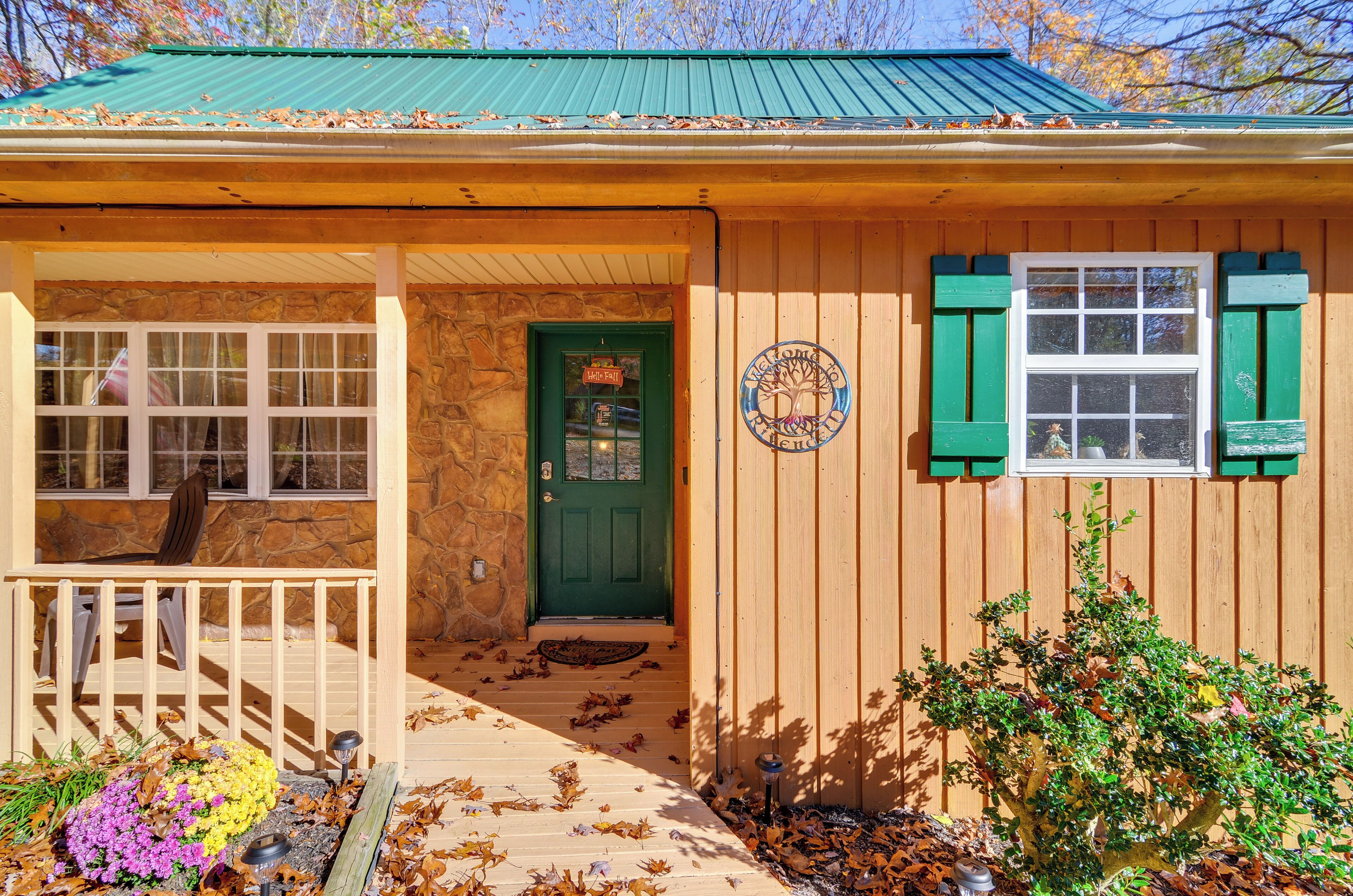 A wooden building with a green door, a stone wall, and a porch with a chair.