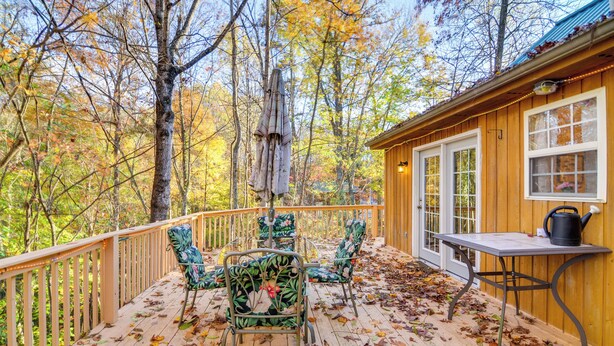 A wooden deck with chairs and a table, surrounded by trees with autumn leaves. - Burnside Resort Cabin w/ Hot Tub & Outdoor Spots! (Burnside)