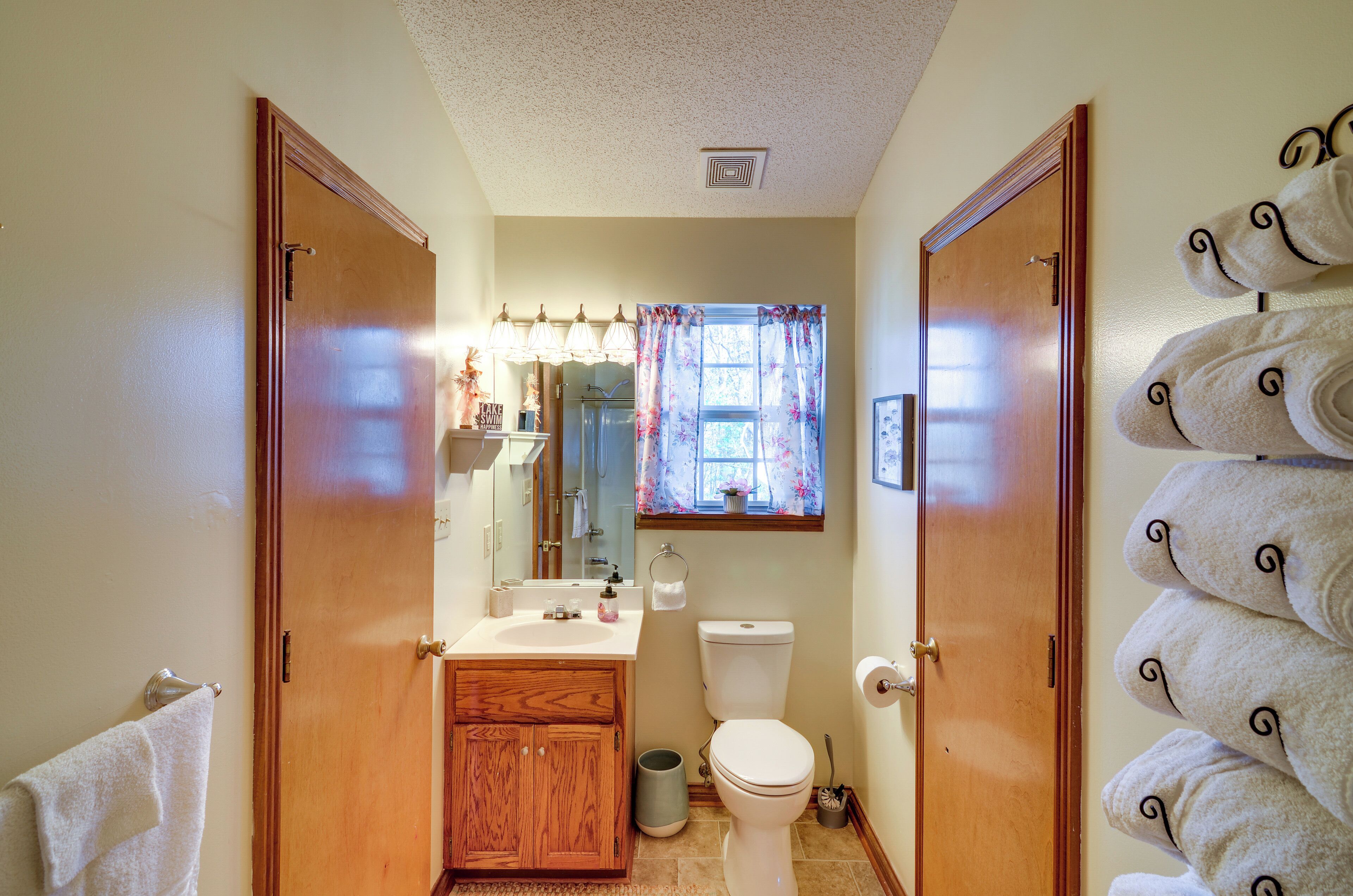 Une salle de bain avec une porte en bois, un lavabo, des toilettes et une fenêtre ornée de rideaux à motifs floraux.