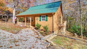 A wooden cabin with a green roof, a porch, and a small garden area. - Burnside Resort Cabin w/ Hot Tub & Outdoor Spots! (Burnside)