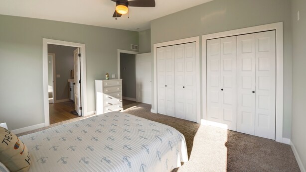 A bedroom with a bed, a ceiling fan, a dresser, and a closet. - Views of Lewis & Clark Lake - Modern Apt w/ Deck (Crofton)