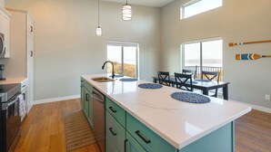 A modern kitchen with a large island, pendant lights, and a dining area with chairs and a table. - Views of Lewis & Clark Lake - Modern Apt w/ Deck (Crofton)