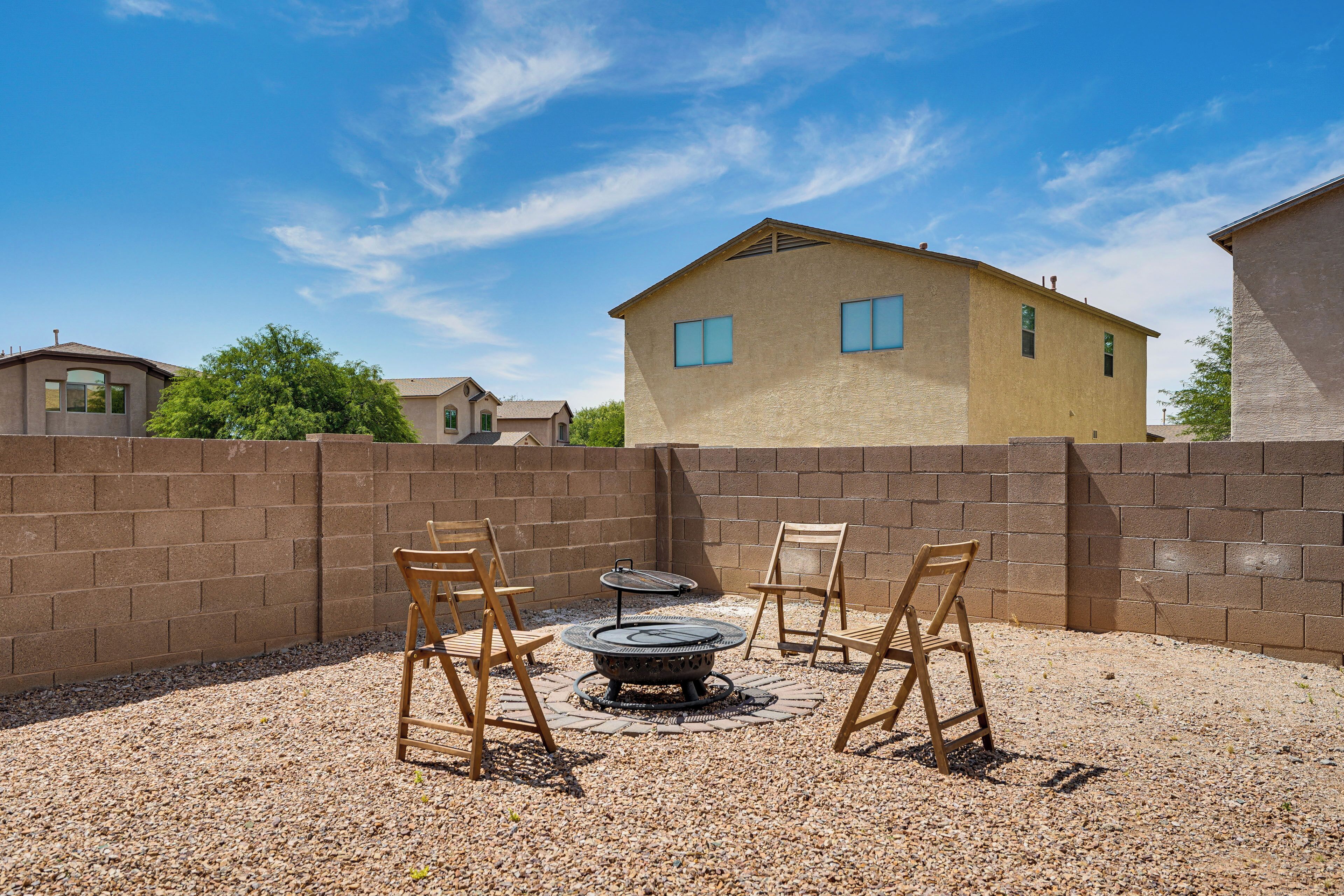A backyard with a fire pit, two wooden chairs, and a brick wall.