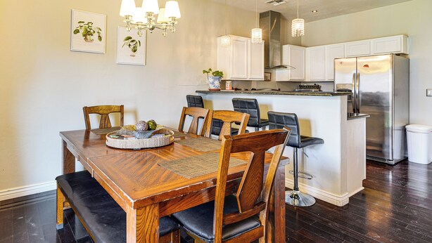 Una cocina moderna con una mesa de comedor de madera, sillas, un refrigerador y lámparas colgantes.
