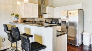 Una cocina con armarios blancos, un refrigerador de acero inoxidable, un microondas y una barra con taburetes negros.