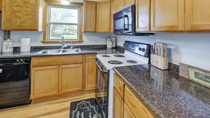 A kitchen with wooden cabinets, a granite countertop, a stove, a microwave, a dishwasher, and a window providing natural light. - Charming Rockland Retreat w/ Deck & Grill! (Bangor)