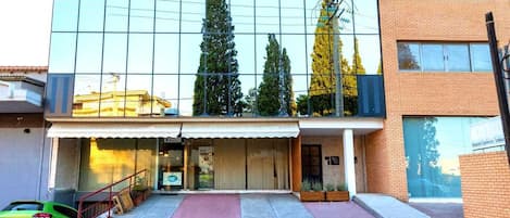 A modern building with large glass windows, a covered entrance, and a green car parked in front.