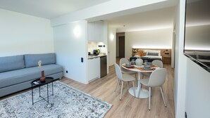 A modern living room with a grey sofa, a small coffee table, and a dining area with a table and chairs. - Athens Airport Living spaces (Spata-Artemida)