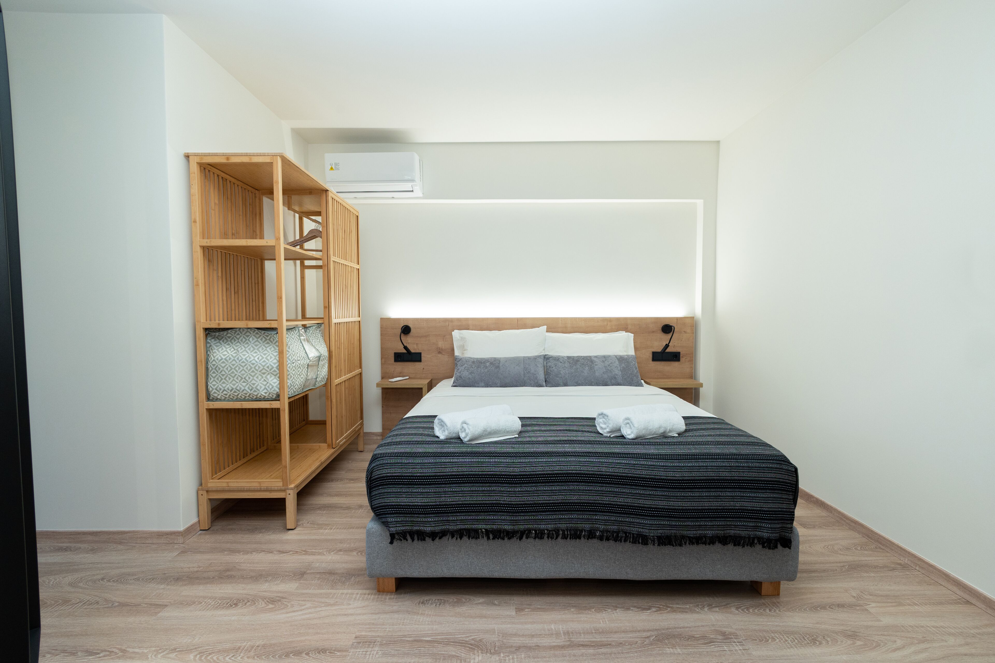 Une chambre à coucher bien rangée, avec un lit, une armoire en bois, une table de chevet et un appareil de climatisation.