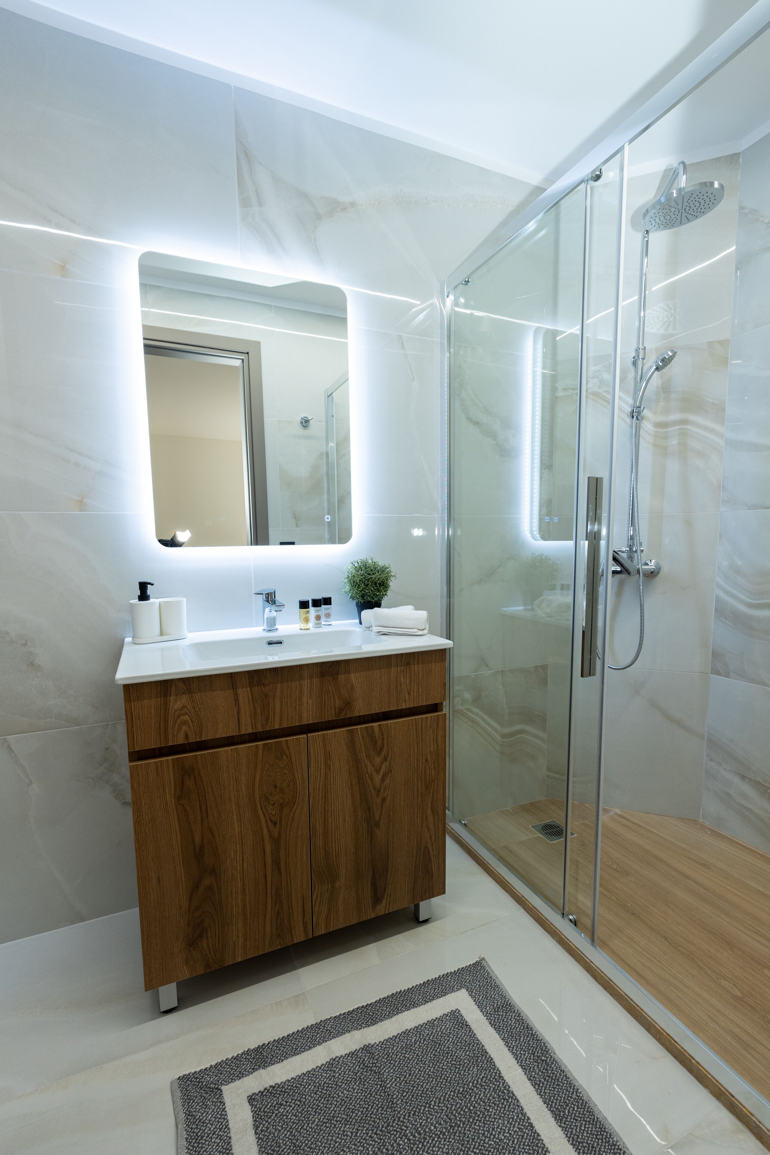 A modern bathroom with a glass-enclosed shower, a wooden vanity, and a marble-tiled wall.