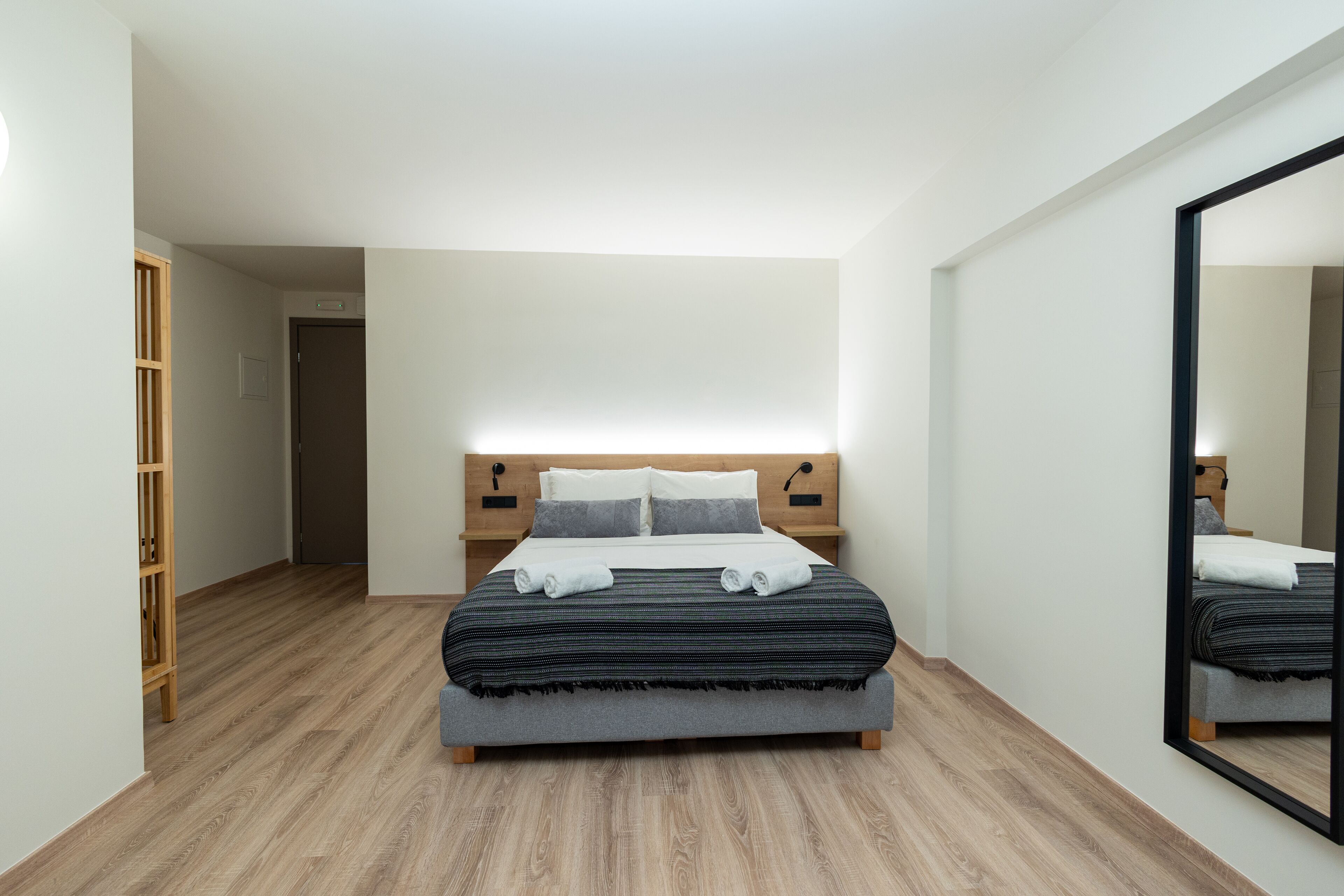 A modern bedroom with a large bed, wooden headboard, and a mirror on the wall.
