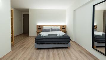 A modern bedroom with a large bed, wooden headboard, and a mirror on the wall.