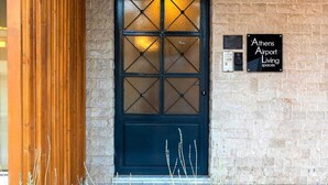 A building entrance with a dark blue door, a stone wall, and a sign for Athens Airport Living Spaces. - Athens Airport Living spaces (Spata-Artemida)