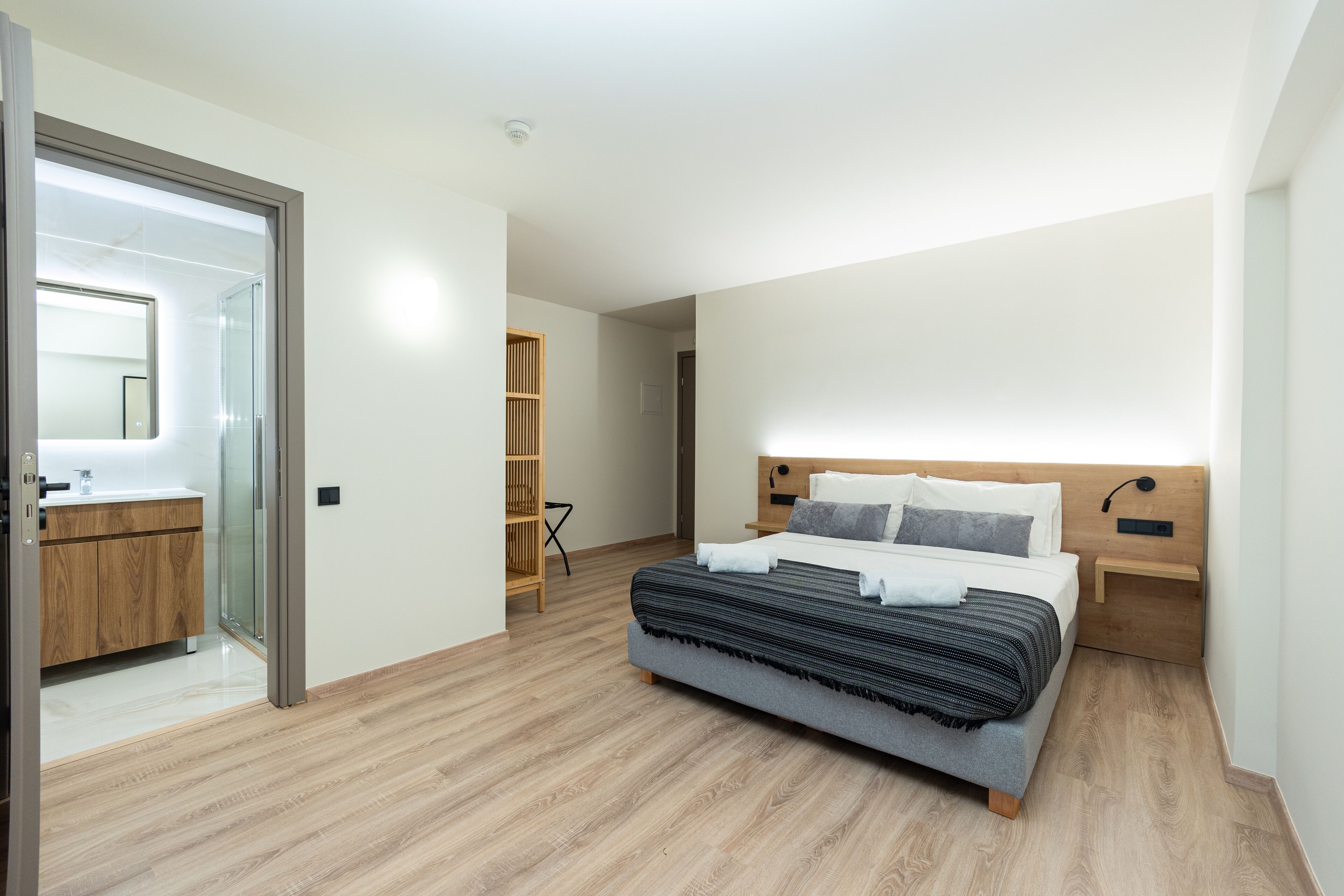 Un dormitorio moderno con una cama grande, cabecera de madera, mesitas de noche y una mampara de ducha de vidrio.