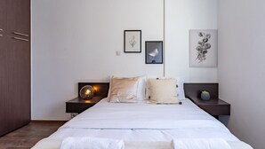 Un dormitorio con una cama grande, dos mesitas de noche, un armario y dos láminas botánicas enmarcadas en la pared.