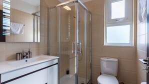 Un baño moderno con ducha envuelta en vidrio, un lavamanos blanco con espejo y un inodoro.