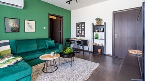 Een moderne woonkamer met een groene bank, een salontafel en een eethoek met een kleine tafel en stoelen.
