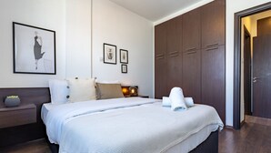 Een moderne slaapkamer met een groot bed, een donker houten garderobe en een nachtkastje met een lamp.