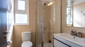 Een moderne badkamer met een douchecabine van glas, een wit toilet, een grote spiegel en een wit wastafelmeubel.