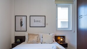A neatly made bed with white linens, a bedside lamp, and a framed picture with the word "love." on the wall. - Harbor 102: Stylish 1-Bedroom Apartment in Larnaca (Cyprus - Larnaca)