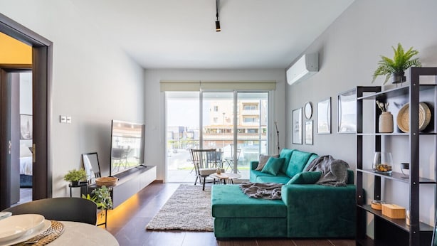 Una sala de estar moderna con un sofá verde, un comedor con mesa dispuesta y un gran ventanal con vistas a la ciudad.