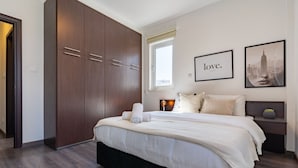 Un dormitorio con una cama grande, un armario, una mesita de noche con lámpara y cuadros enmarcados en la pared.