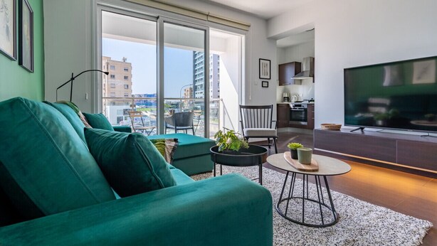 Una sala de estar moderna con un sofá verde, una mesita redonda y un televisor.