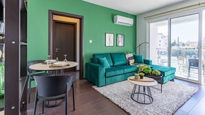 Una sala de estar moderna con una pared verde, un sofá color turquesa, una mesa de comedor con sillas y un ventanal con vistas a la ciudad.