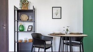 Un comedor con una mesa redonda, sillas negras, una estantería de metal negra con objetos decorativos y un cuadro en la pared.