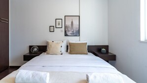 Habitación de hotel moderna con una cama grande, dos mesitas de noche y una imagen enmarcada de un paisaje urbano en la pared.