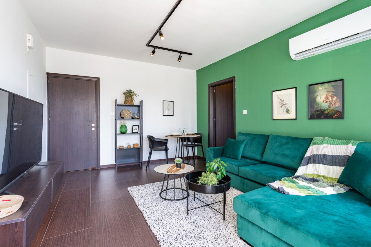 A modern living room with a teal sofa, a coffee table with plants, a dining area with chairs, and artwork on the walls.