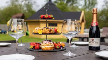 A picnic setup with a three-tiered dessert stand, two wine glasses, and a bottle of Duchessalia Fragolino wine on a wooden table.