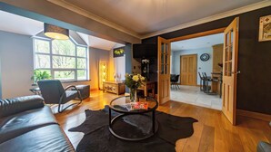 Una sala moderna con un sofá de cuero, una mesa de centro de vidrio y un tapete negro. Se ve un comedor a través de una puerta abierta.