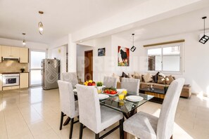 Eine moderne Küche mit Kühlschrank, Backofen und Essbereich mit Glastisch und Stühlen.