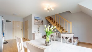 A spacious living area with a dining table, chairs, a vase of flowers, a staircase, and a painting on the wall. - Ferienwohnung am Meer, Urlaub auf der Insel Usedom, Apartment Bianco 49 (Świnoujście)
