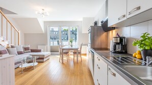A modern kitchen with a dining area, wooden flooring, and a view through the window. - Ferienwohnung am Meer, Urlaub auf der Insel Usedom, Apartment Bianco 49 (Świnoujście)