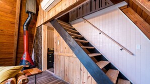 A wooden interior with a staircase, a red chimney, and a bed with striped bedding. - A-Frame of Mind - Time to Kick Back and Relax (Demorest)