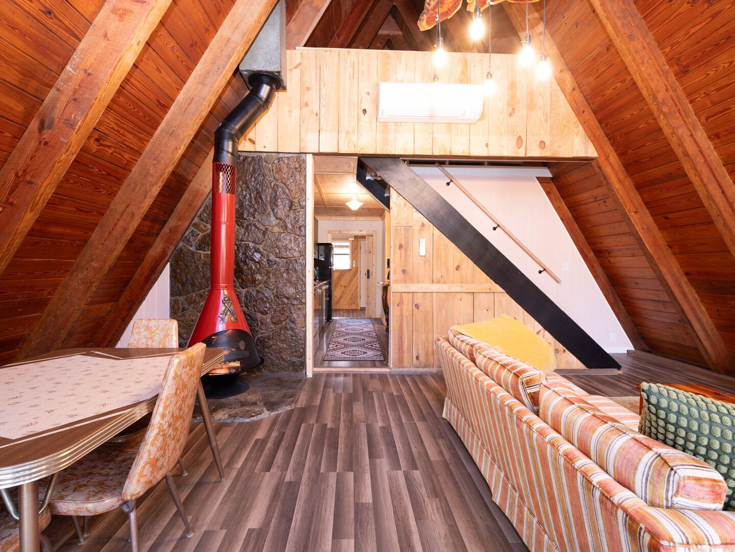 An attic room with a fireplace, wooden beams, a dining table, and a sofa.