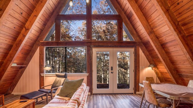 A cozy attic room with a wooden sloped ceiling, a large window, a sofa, a dining table with chairs, and a lamp. - A-Frame of Mind - Time to Kick Back and Relax (Demorest)