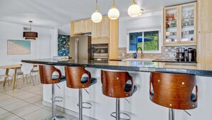 Une cuisine moderne dotée d’un îlot central, de tabourets de bar, d’appareils électroménagers en acier inoxydable et d’armoires en bois.
