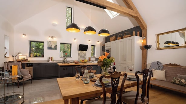 Une cuisine spacieuse de style loft, avec un coin repas, des poutres en bois, des luminaires suspendus et une vue sur l’extérieur.