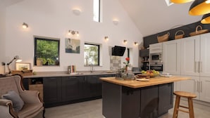 Une cuisine moderne dotée d’un grand îlot central, de meubles de rangement aux couleurs sombres et d’un coin repas avec une chaise rembourrée.
