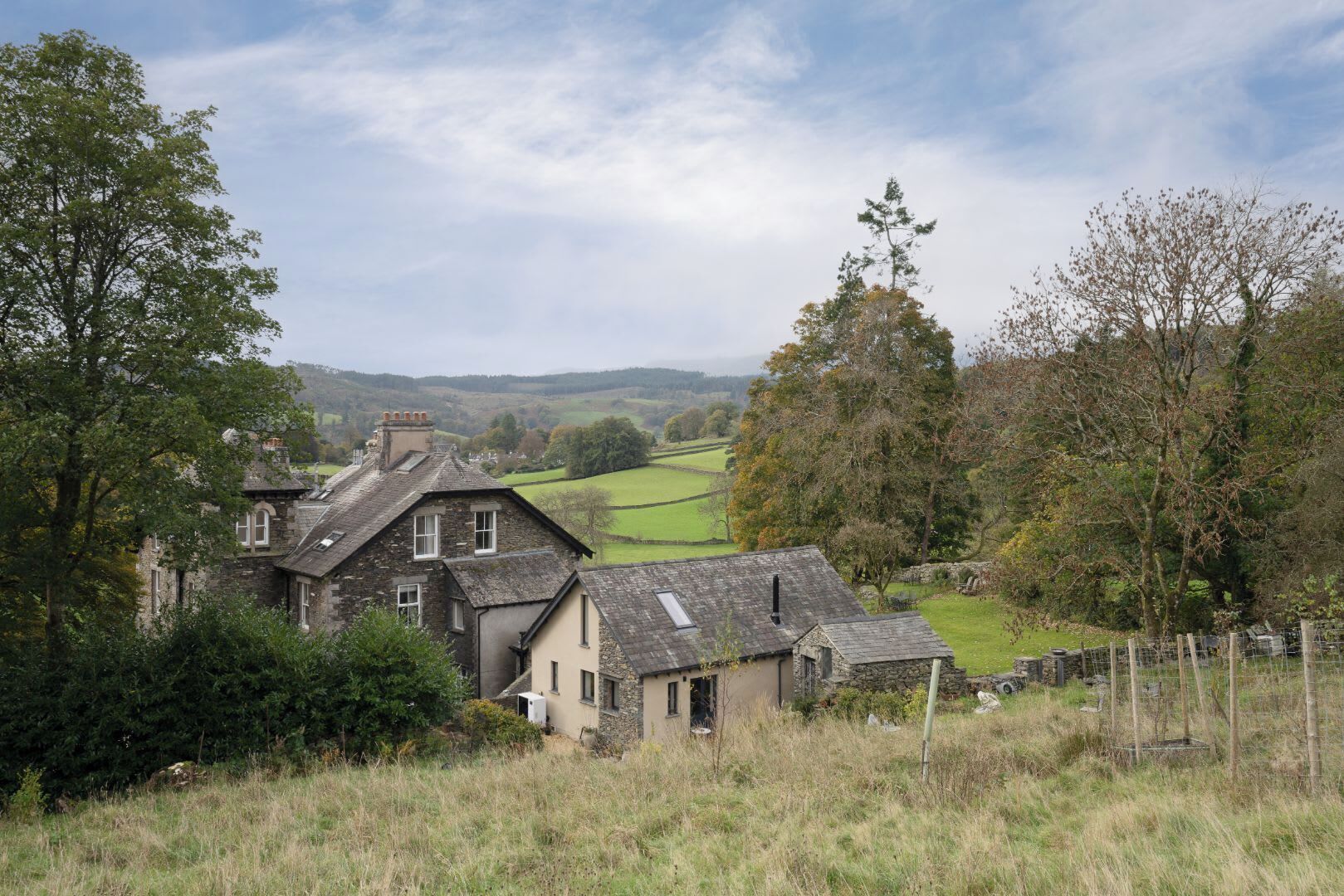 Une maison en pierre avec un toit en pente, entourée d’un paysage rural composé de champs et d’arbres.