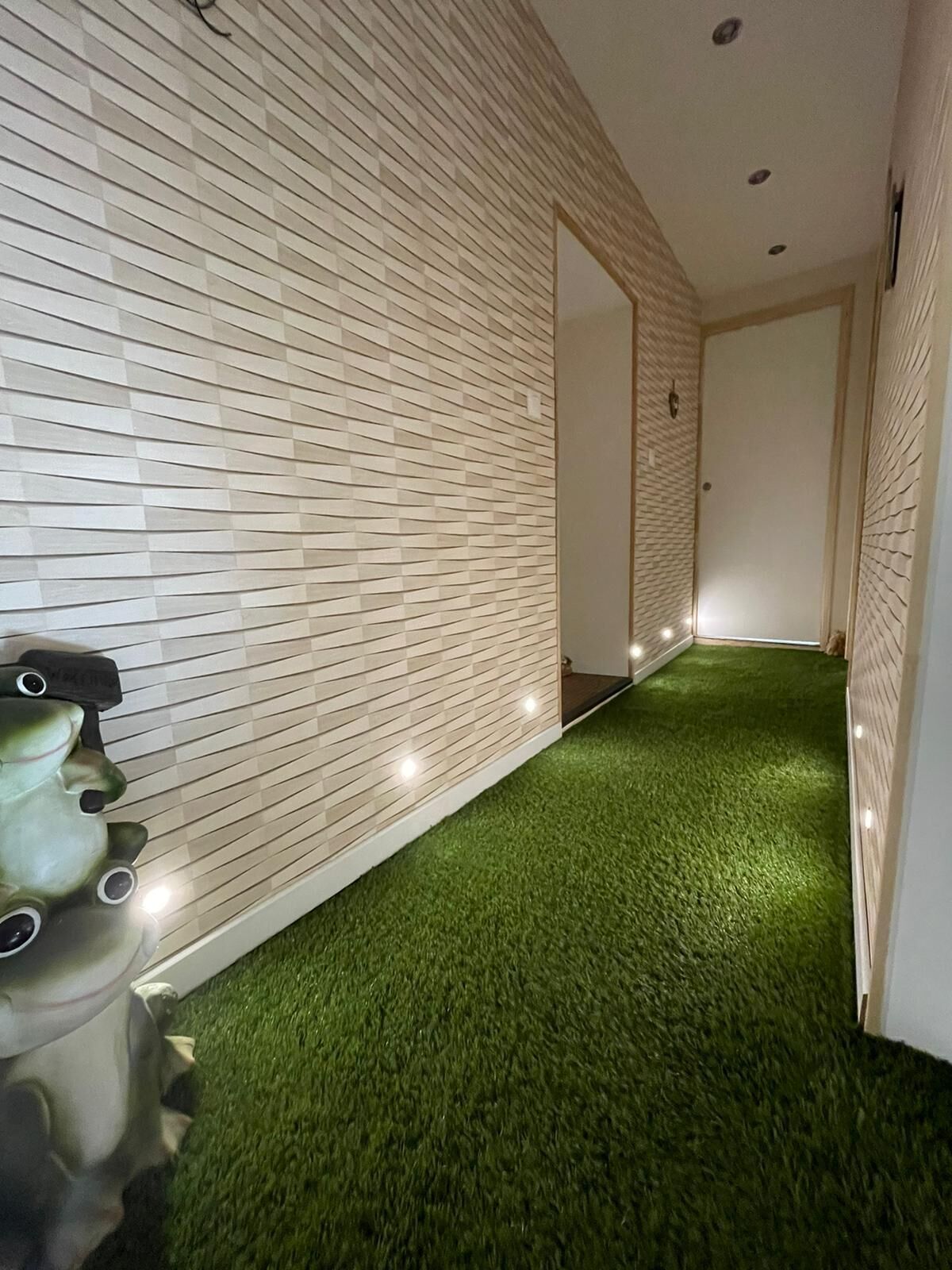 Een gang met een vloer van groen kunstgras en een witte bakstenen muur.