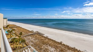Blick auf einen Strand vom Balkon aus, mit Pool, Palmen und Sandstrand.