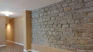 A room with a stone wall, wooden flooring, and recessed ceiling lights. - RMaison Luxury Suites Olbia  (Olbia)
