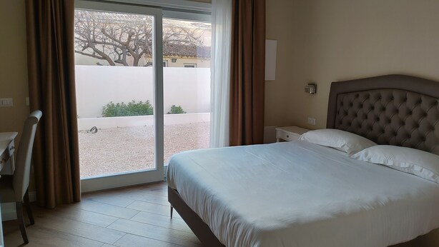 A hotel room with a bed, a nightstand, a chair, and a window with curtains. - RMaison Luxury Suites Olbia  (Olbia)